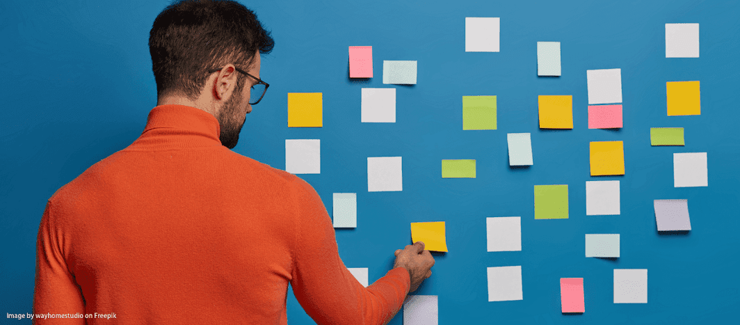 Homme de dos plaçant des notes adhésives colorées sur un mur, pour un plan d'action