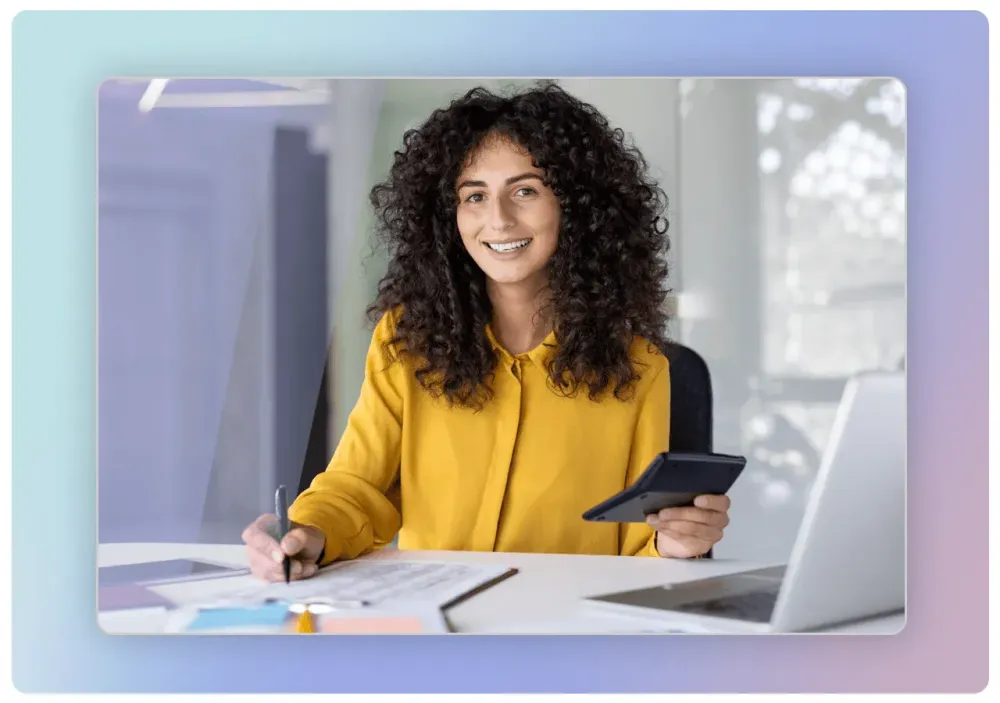 Femme souriante assise à son bureau, une tablette à la main