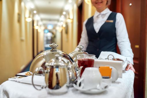 Femme de chambre en tenue portant un plateau de service dans un couloir d'hôtel